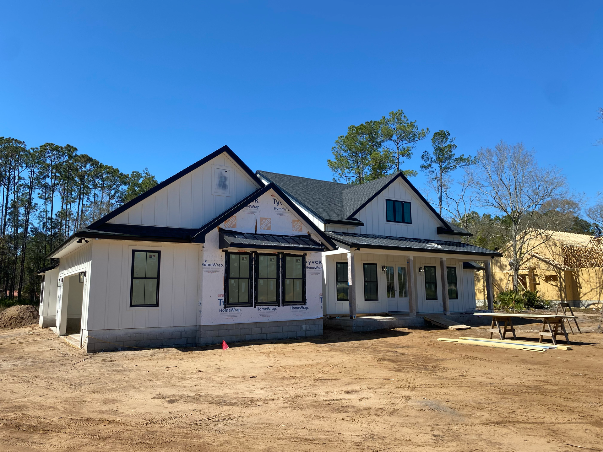 Single-story house with white siding and black roof in a sandy yard under a blue sky.