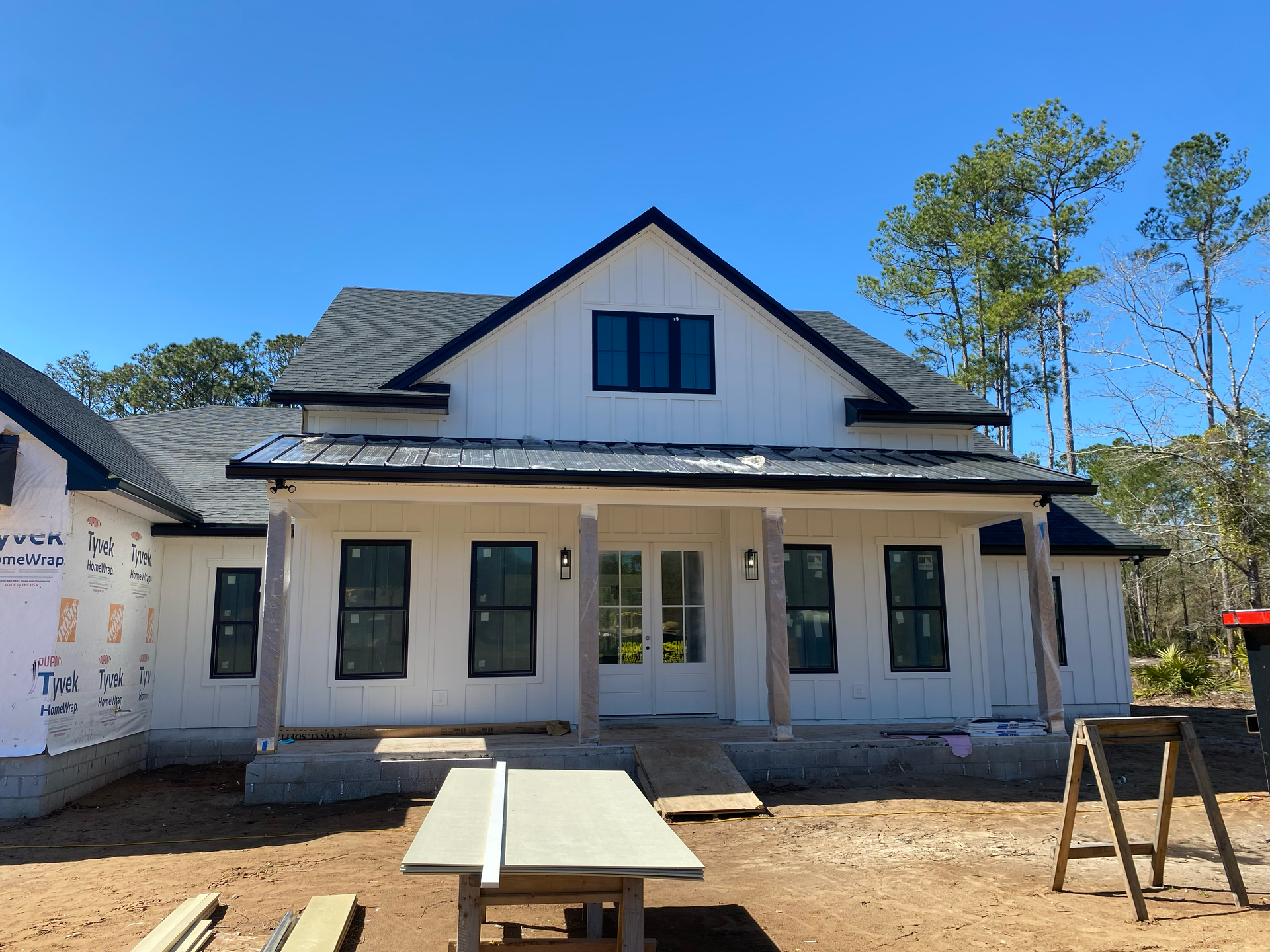 New white house under construction with black roof and front porch, viewed from the yard