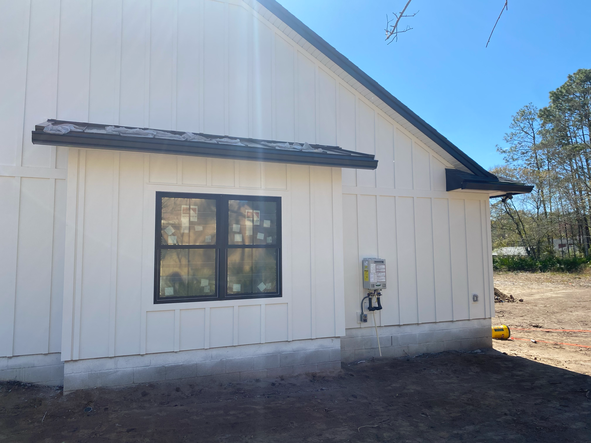 White building exterior with a black-framed window and metal awning under a clear blue sky.
