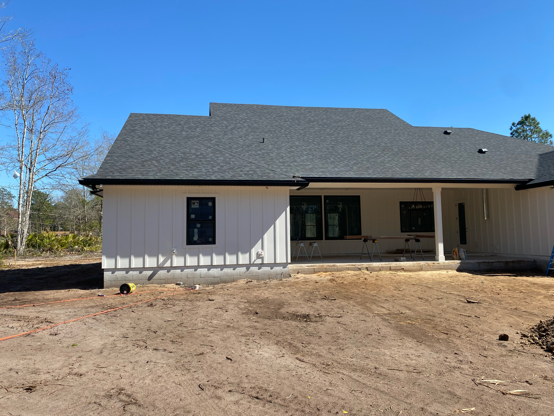 New single-story house with gray siding and a dark roof, viewed from a dirt front yard