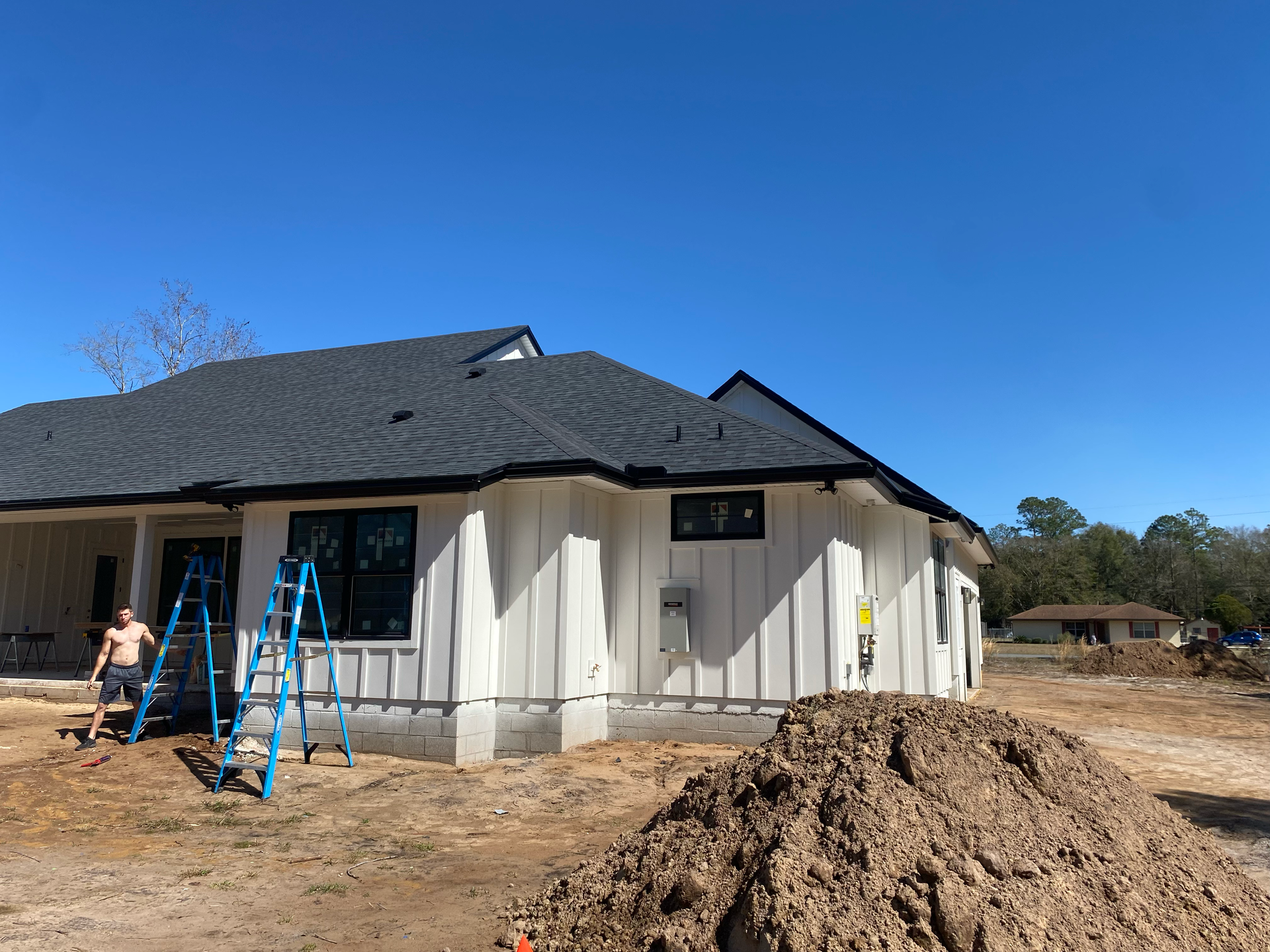 Single-story house under construction with blue ladders and a dirt mound in front