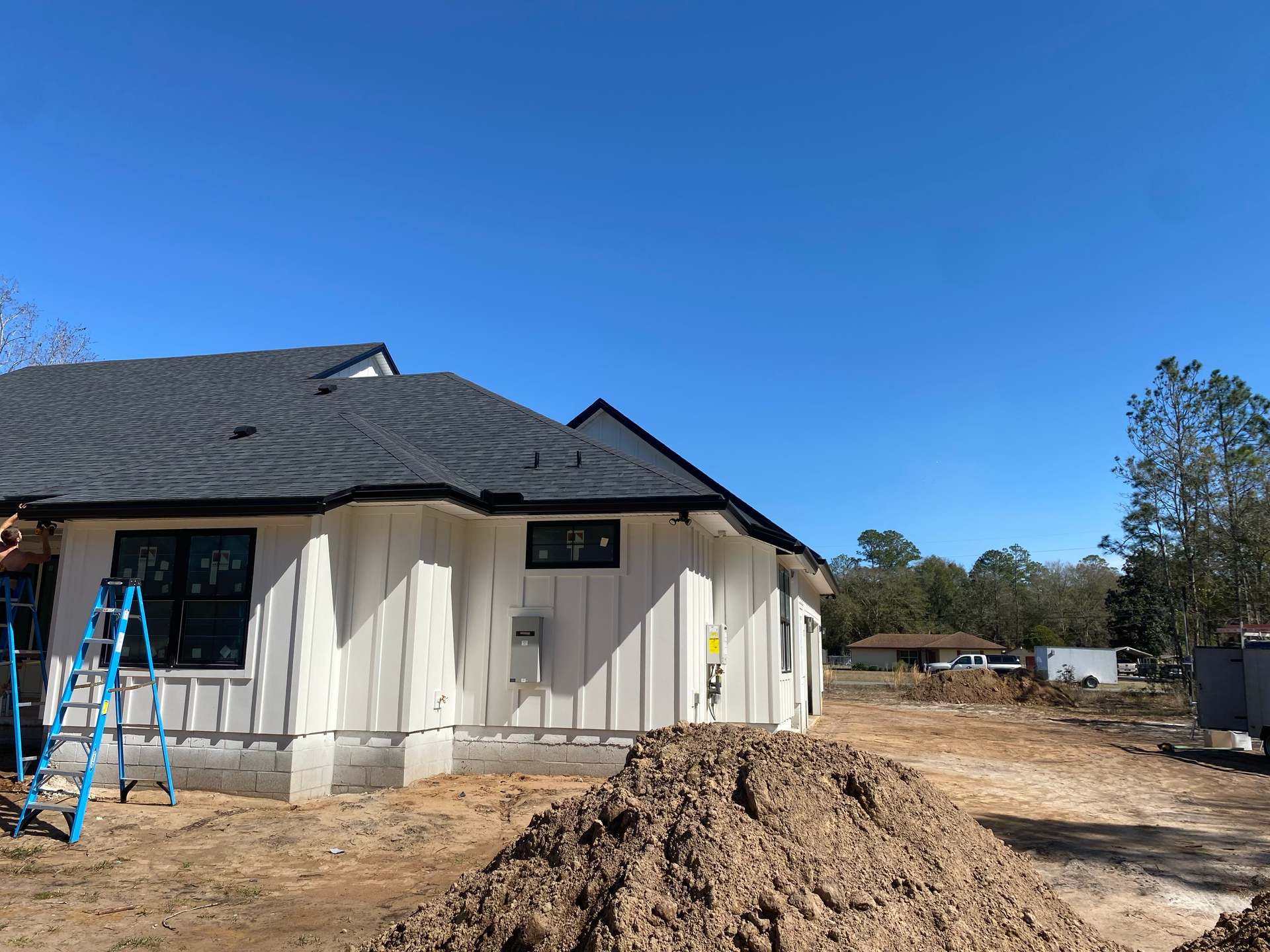 House exterior under construction with blue ladder, dirt pile, and clear sky