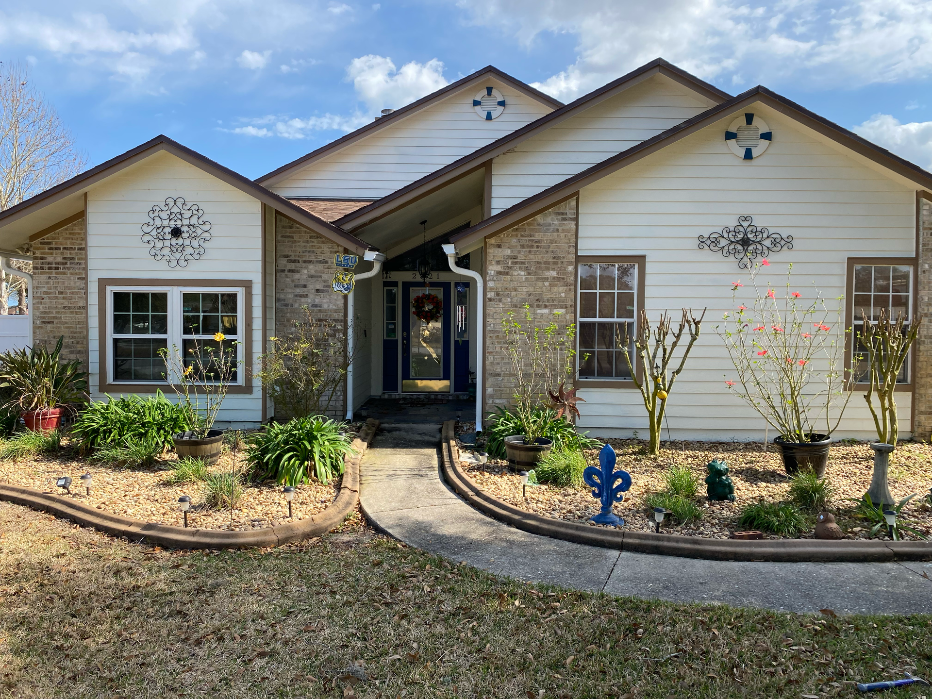 Single-story house with gray and white exterior, front walkway, and landscaped yard under a blue sky