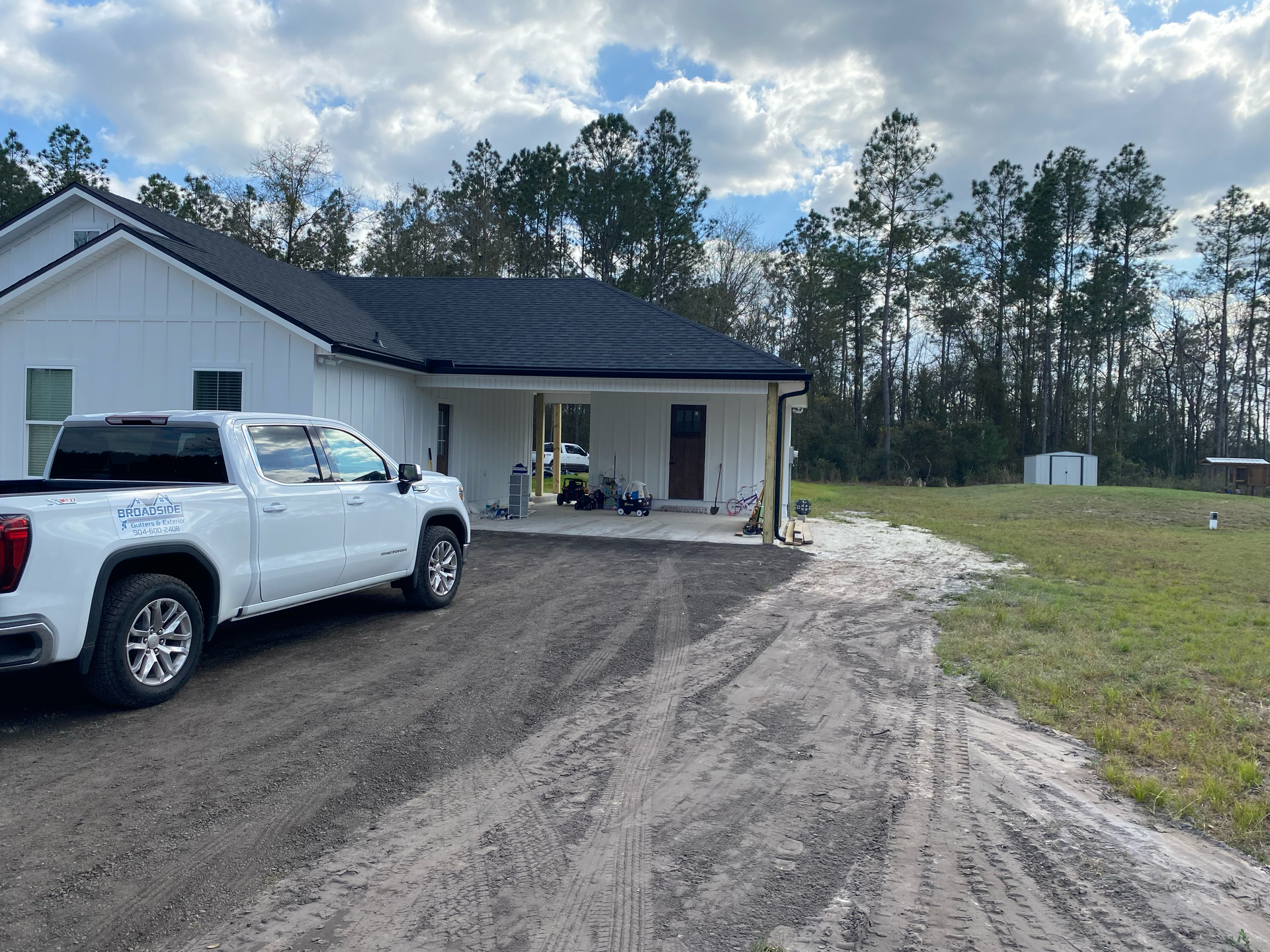 White pickup truck parked beside a new white house with a covered porch and gravel driveway under cloudy skies