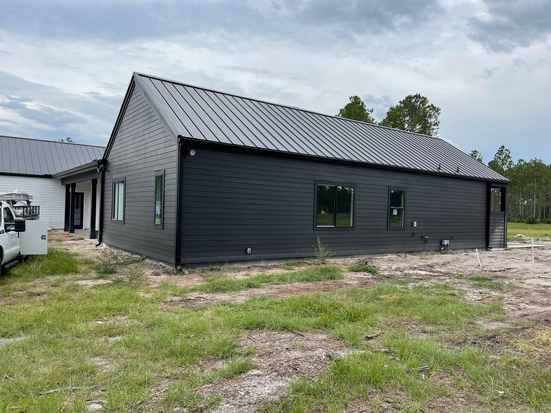 New black siding house with metal roof on a bare construction lot under cloudy sky