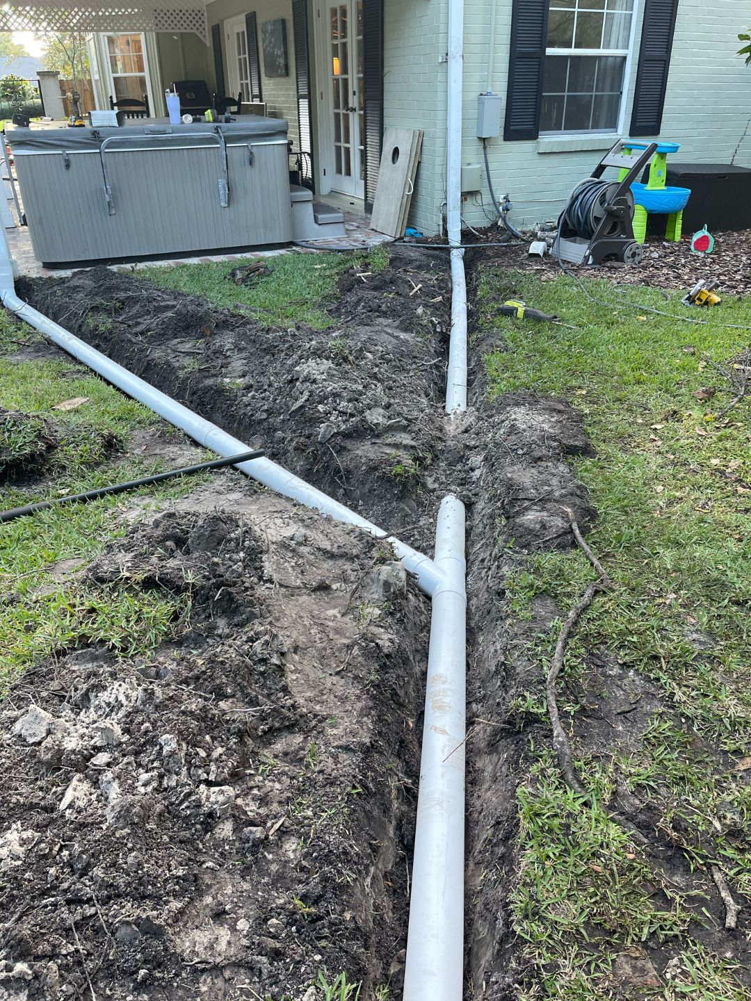 Damaged white downspout pipes along muddy yard beside a house and porch