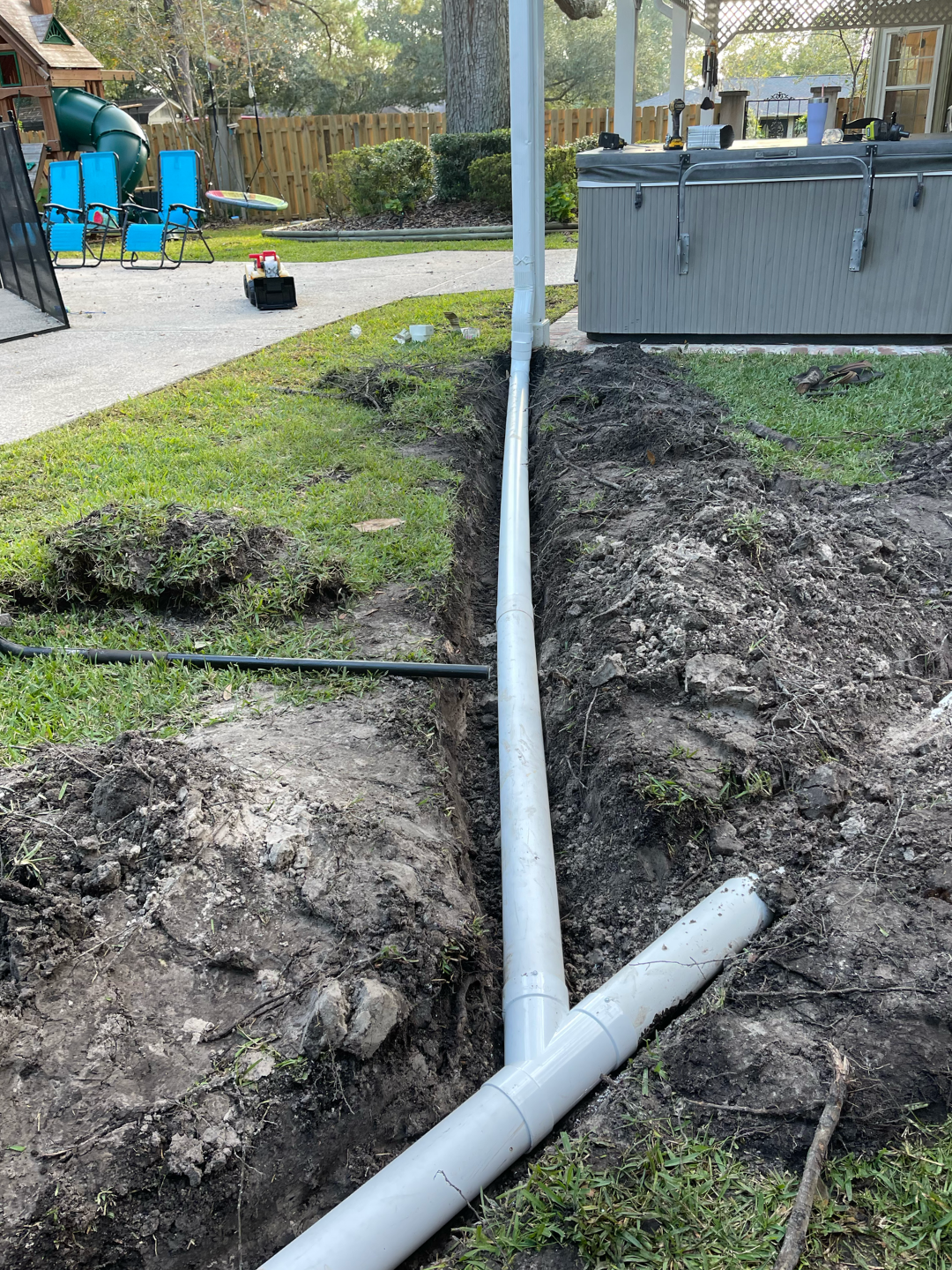 Trenched yard with white utility conduit running underground beside a gray utility box and grass.