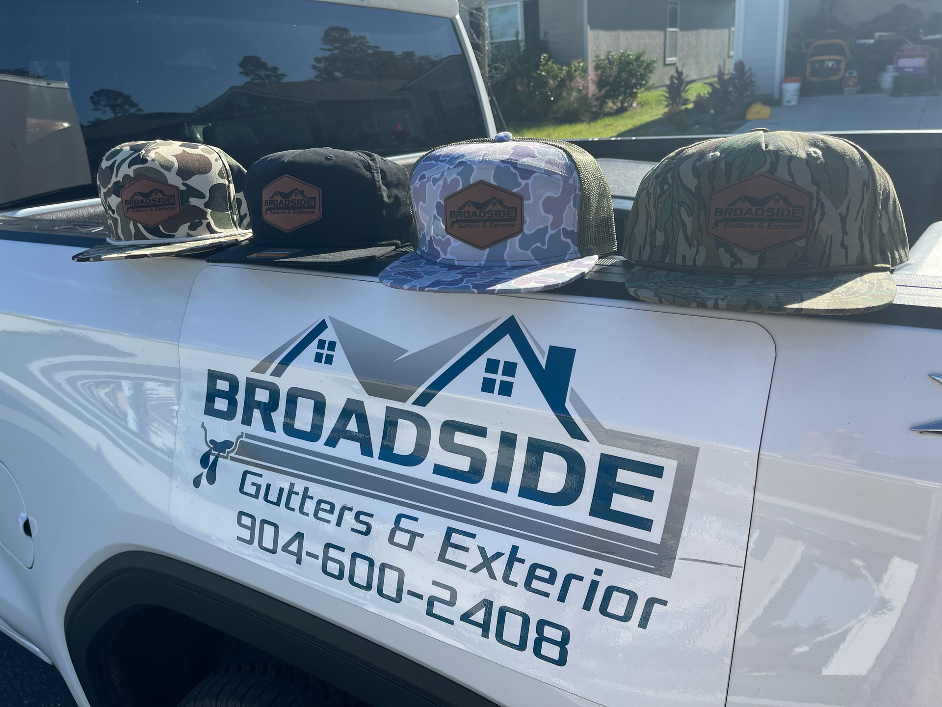 Pickup truck door with Broadside Gutters & Exterior logo and phone number, with hats lined on the roof