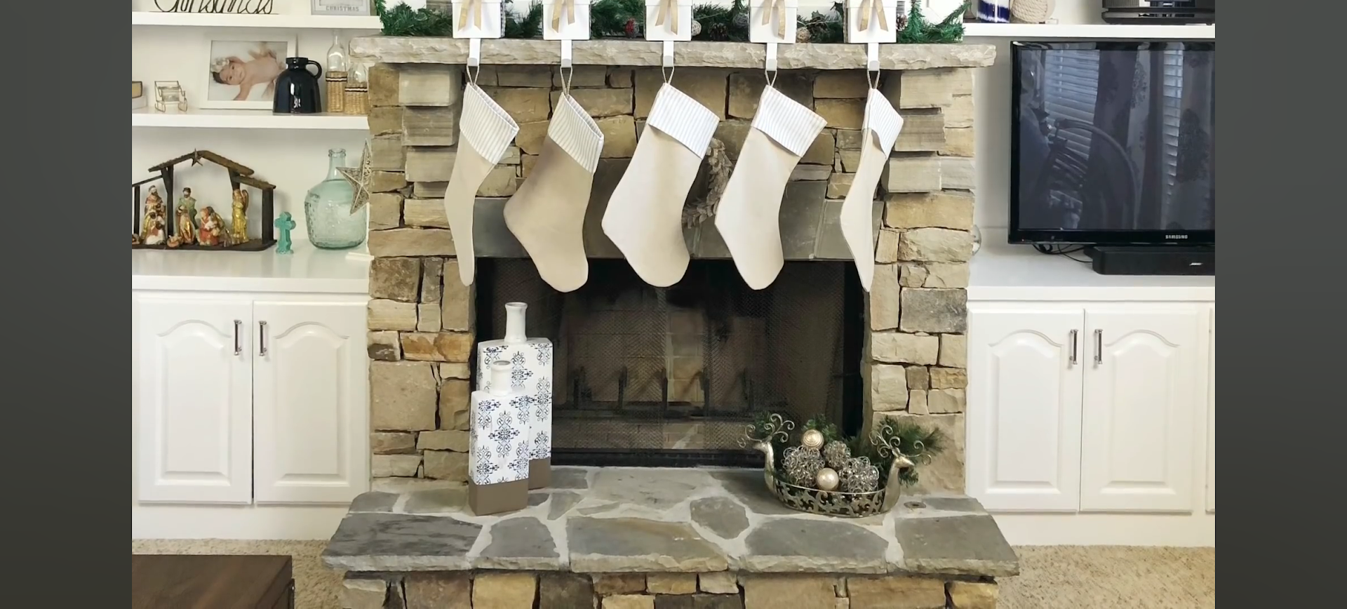 Fireplace with Christmas stockings hanging above, flanked by cabinets and a TV.