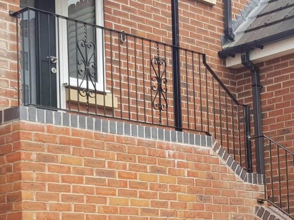 Black metal railings stepping up beside a brick front path, with decorative scroll panels