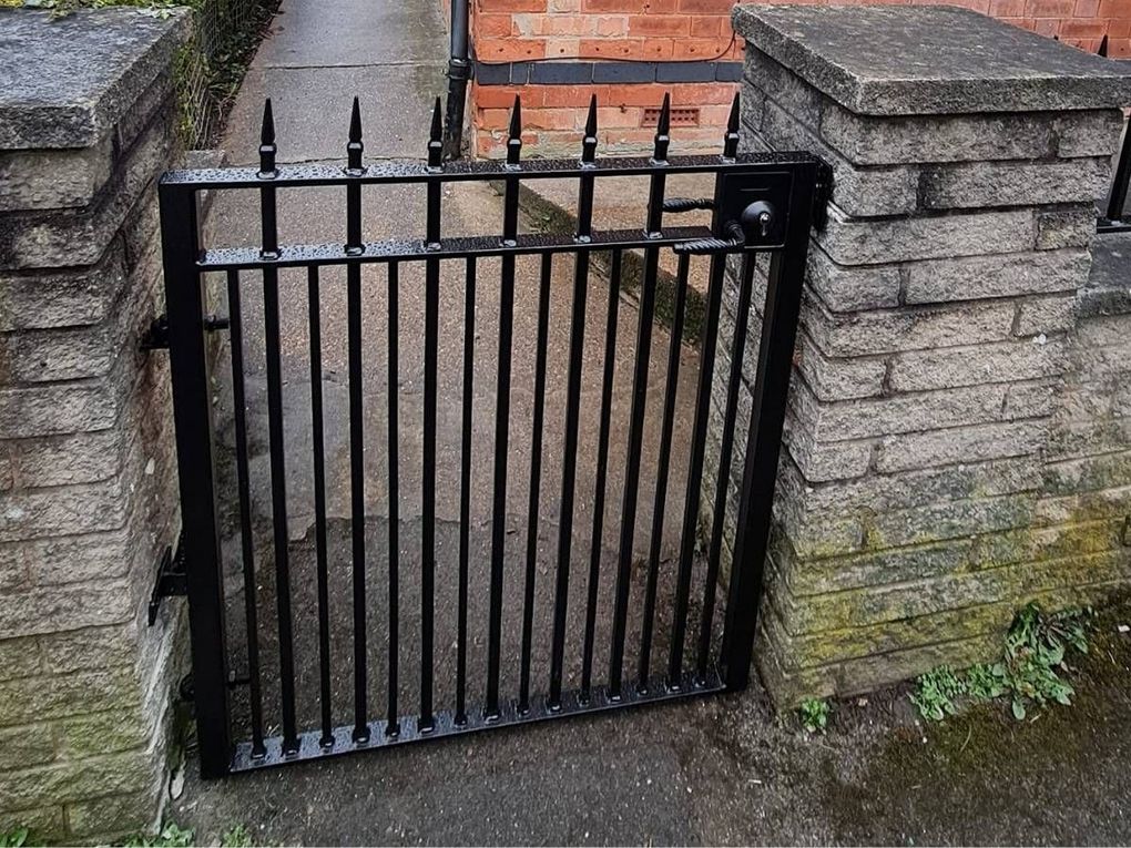 Black spike-top metal side gate hung between two stone pillars