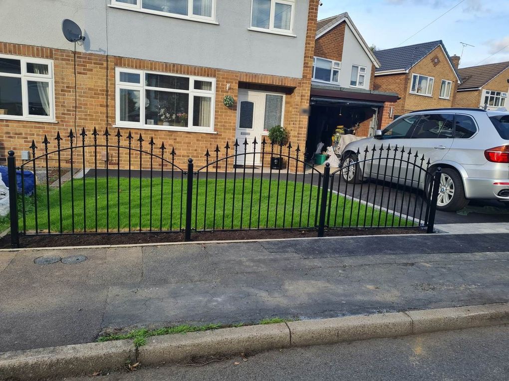 Black railing panels with arched top rails and fleur de lis heads, fixed between ball-top posts along a front garden in Spondon