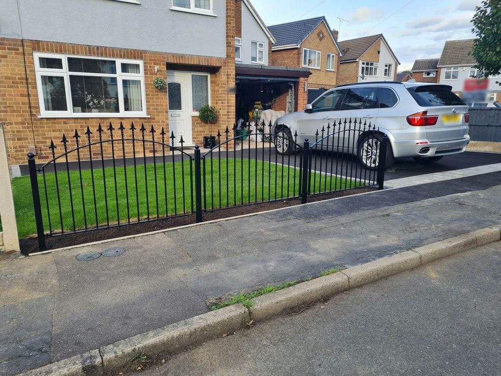 Three arched-top black railing panels with fleur de lis heads along a front lawn beside a driveway