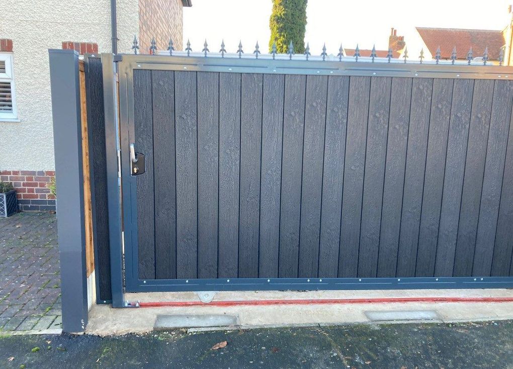 Black composite sliding driveway gate with a row of spear tops, closed across a drive