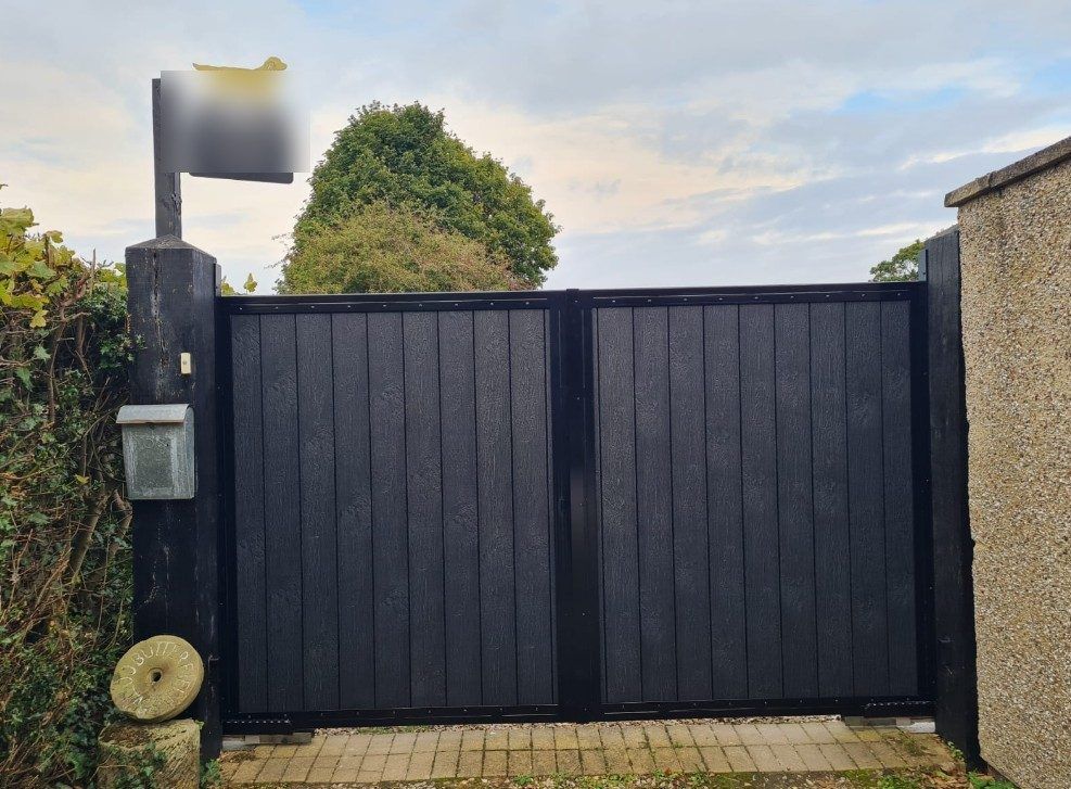 Pair of black composite swing gates hung between timber posts at the entrance to a drive