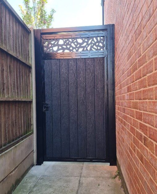 Black composite side gate with a laser-cut decorative top panel in a narrow side passage