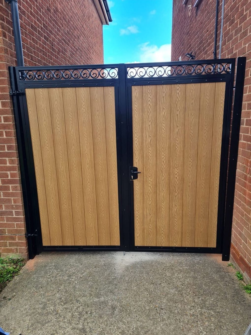 Oak-effect composite double gates in a black steel frame with fishtail toppers along the top