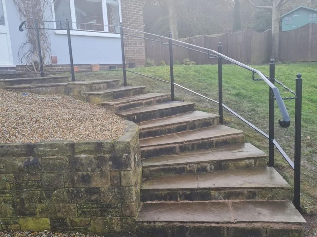 Black post-mounted metal handrail following a curved flight of stone garden steps