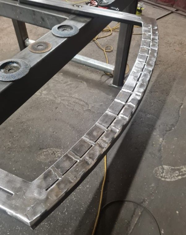 Steel frame for an arched gate being fabricated on the workshop floor, with the curved top rail tacked in place