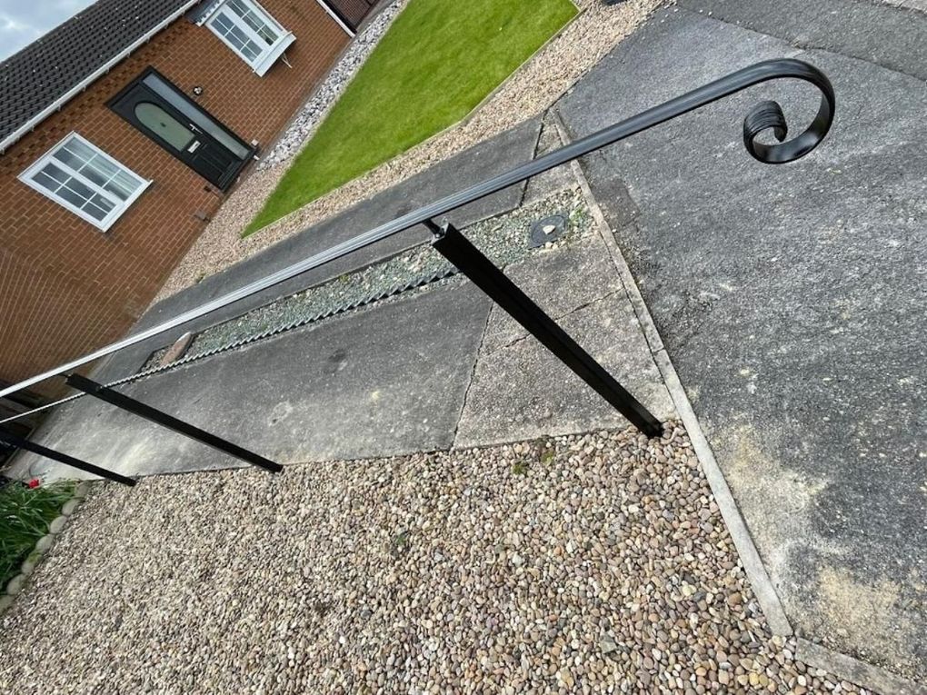 Black metal handrail with a scrolled end running down a sloping front garden path
