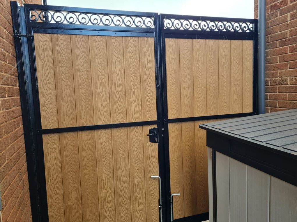 Oak-effect composite double gates with a black scrolled top rail, fitted in the same side passage