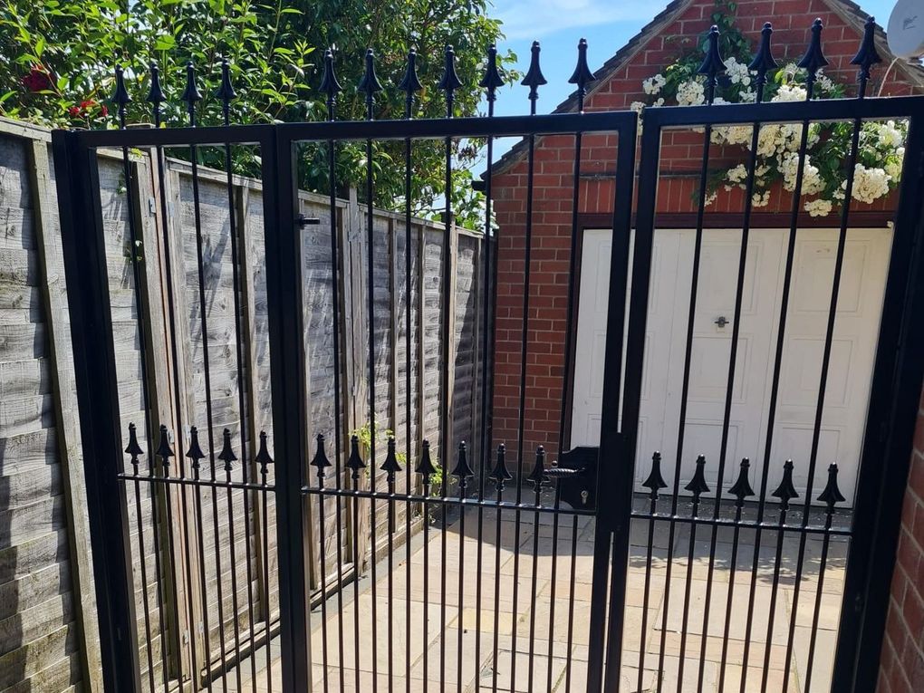 Pair of traditional black spear-top metal gates with dog bars across a courtyard entrance