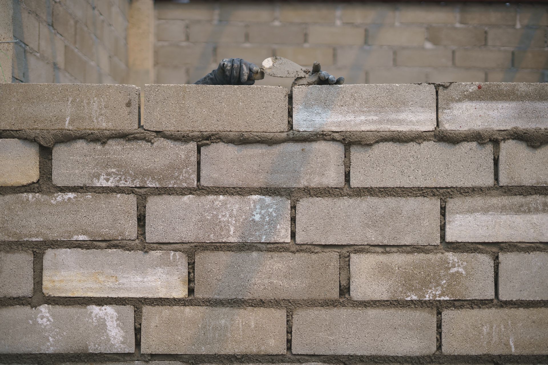 Close-up of gray cinder block wall under construction with gloved hands placing blocks.