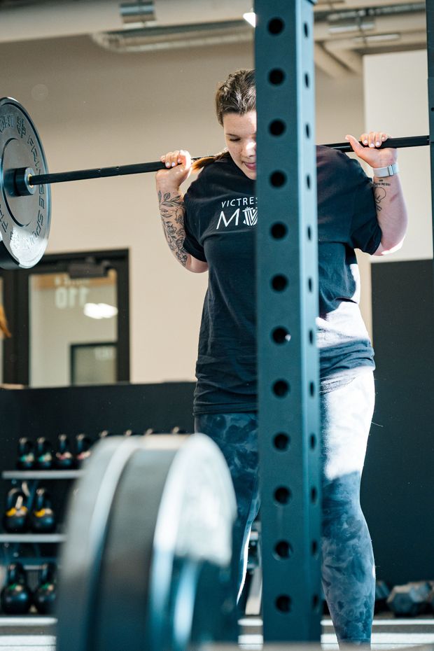 Woman in gym lifting dumbbells overhead. Black shorts, white top, and sneakers.