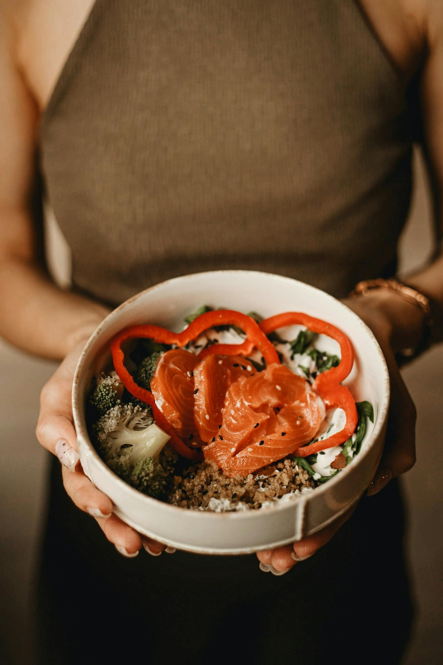 Hands holding a bowl of rice, greens, and sliced tomatoes topped with red sauce.