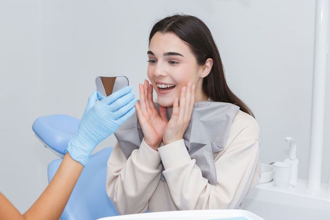 Woman smiling in a dentist chair as a gloved clinician shows her a tooth shade guide