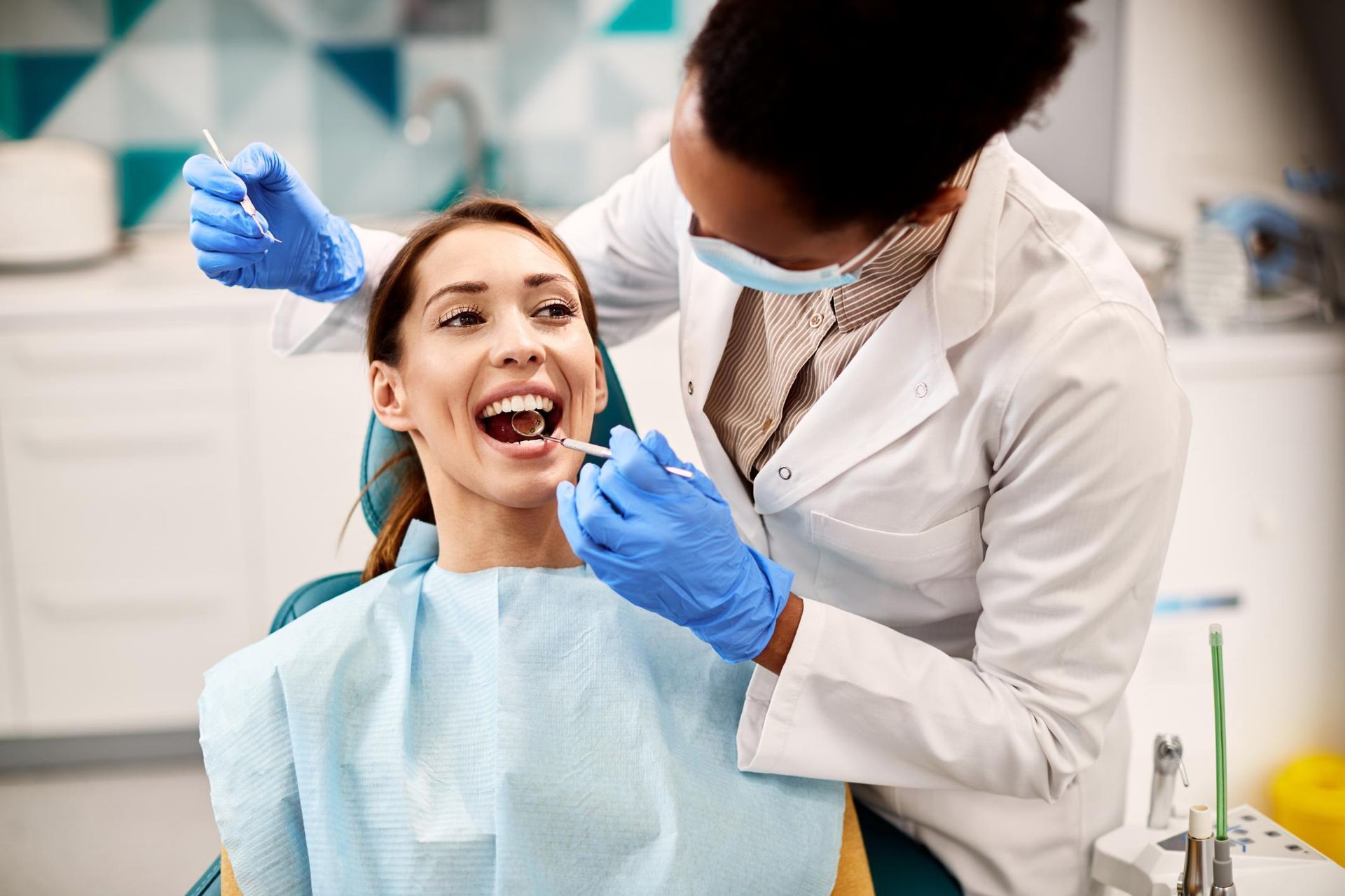 A woman is sitting in a dental chair while a dentist examines her teeth.
