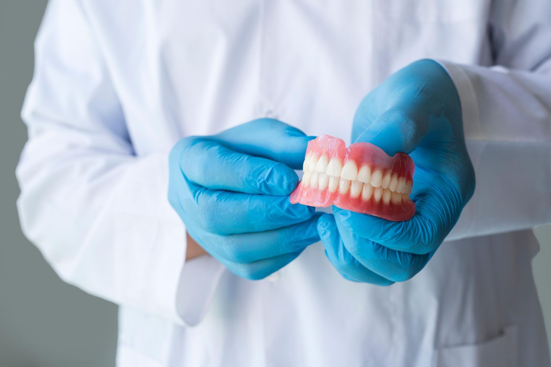 A dentist wearing blue gloves is holding a denture in his hands.