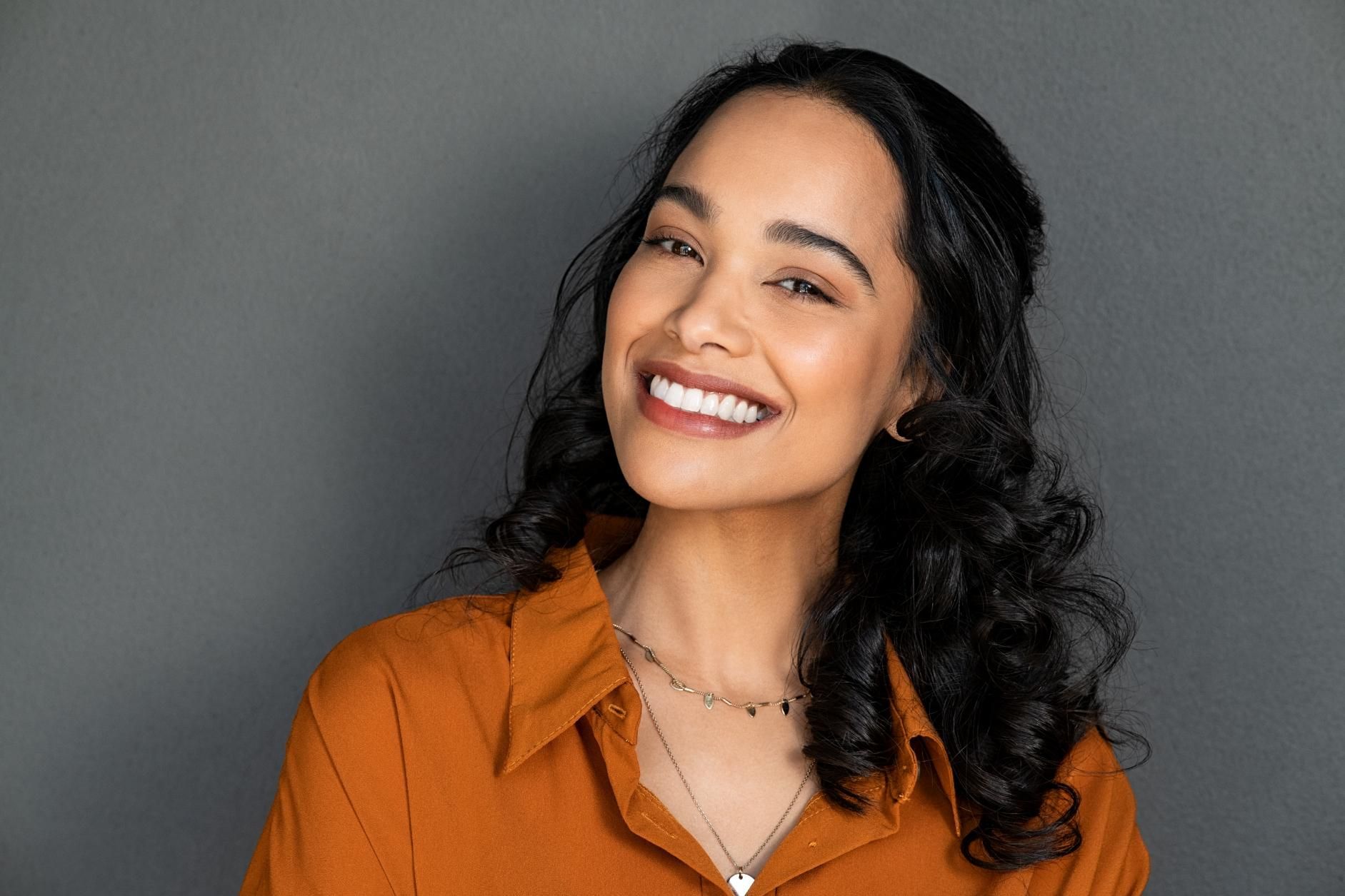 A woman in an orange shirt and necklace is smiling for the camera.