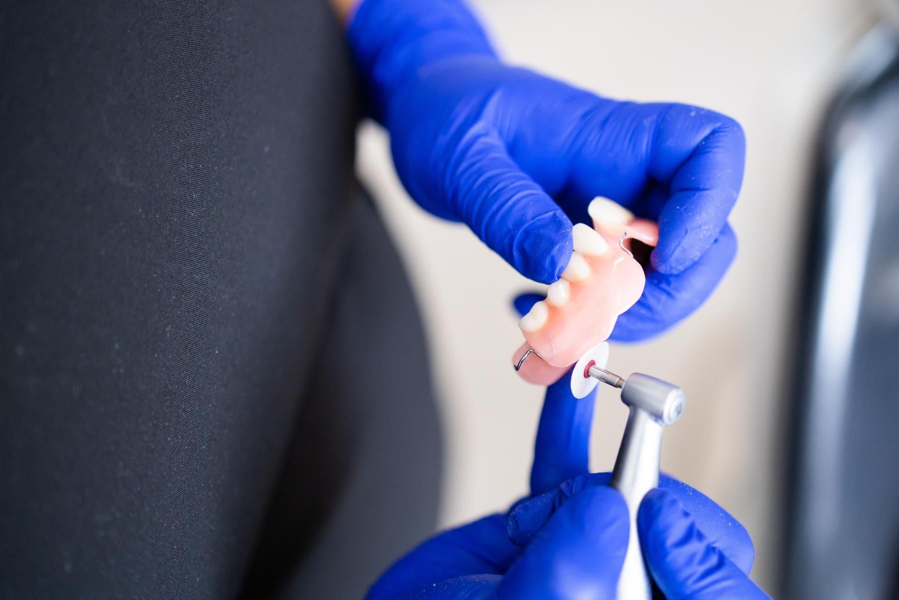 A person is cleaning a denture with a toothbrush in a sink.