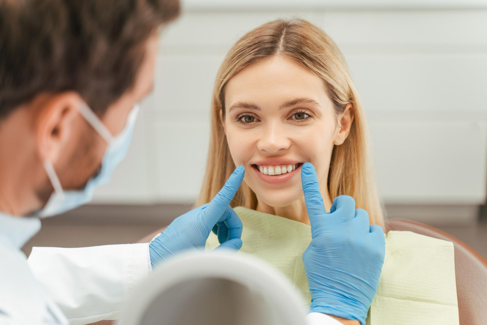 A woman is sitting in a dental chair while a dentist examines her teeth.