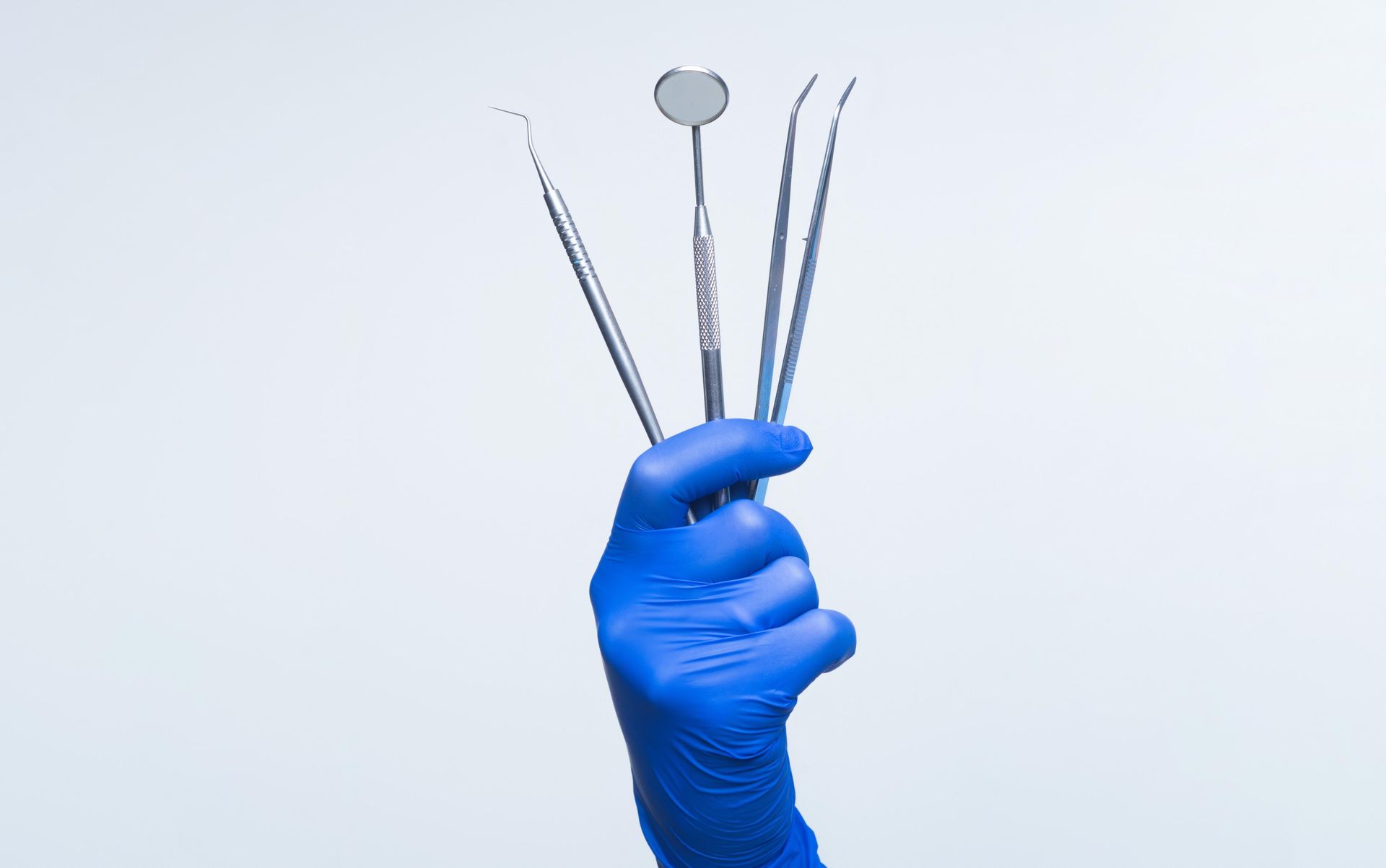 A person wearing blue gloves is holding a set of dental instruments.