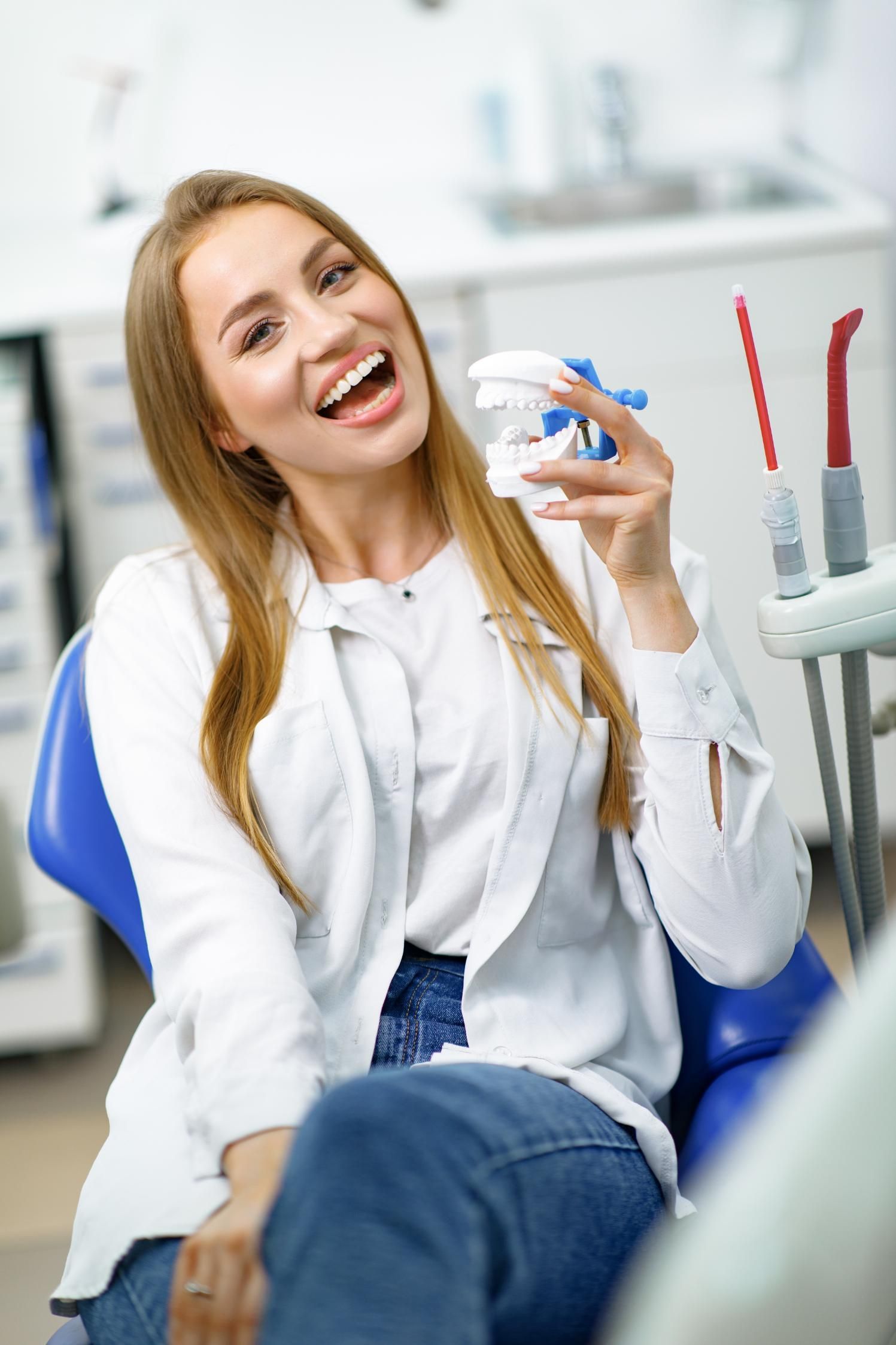 A woman is sitting in a dental chair holding a model of her teeth.