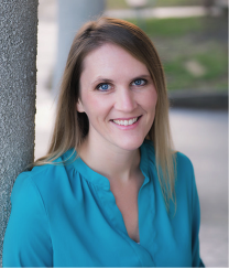 A woman in a blue shirt is smiling and leaning against a pole.