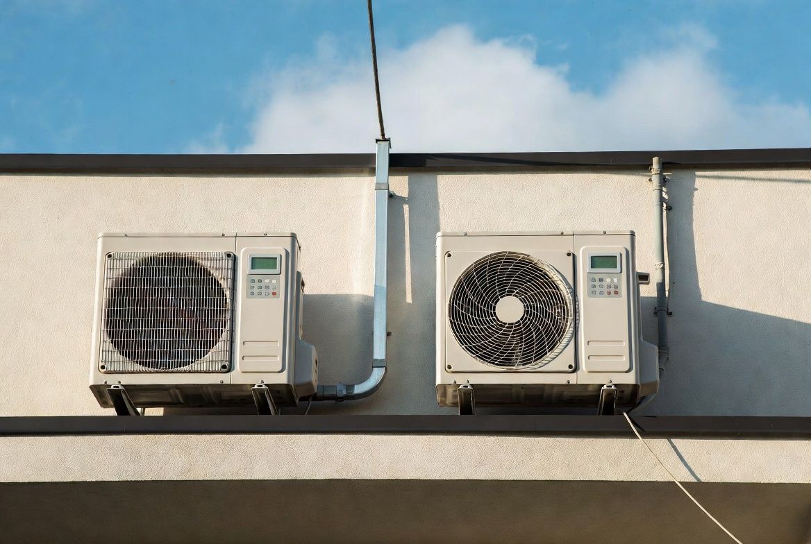 Two outdoor air conditioner units mounted on a building wall under a blue sky.