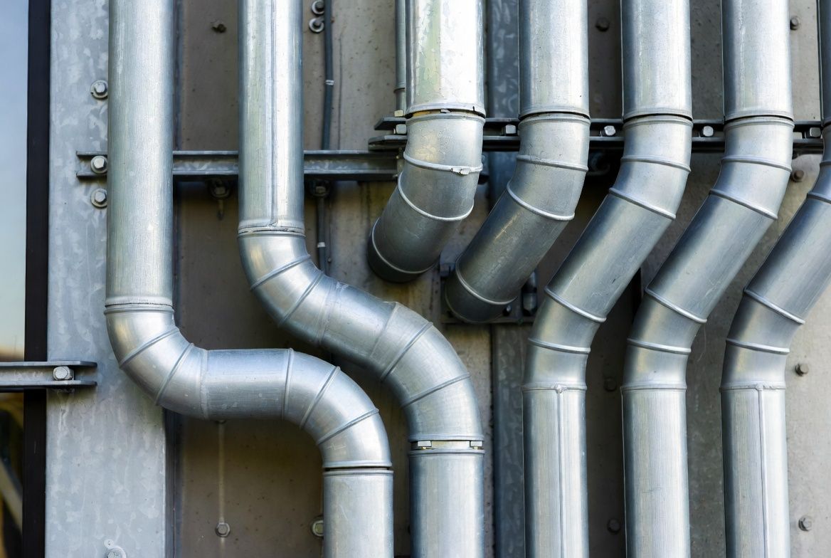 Metal pipes and silver ductwork with multiple bends mounted against a wall