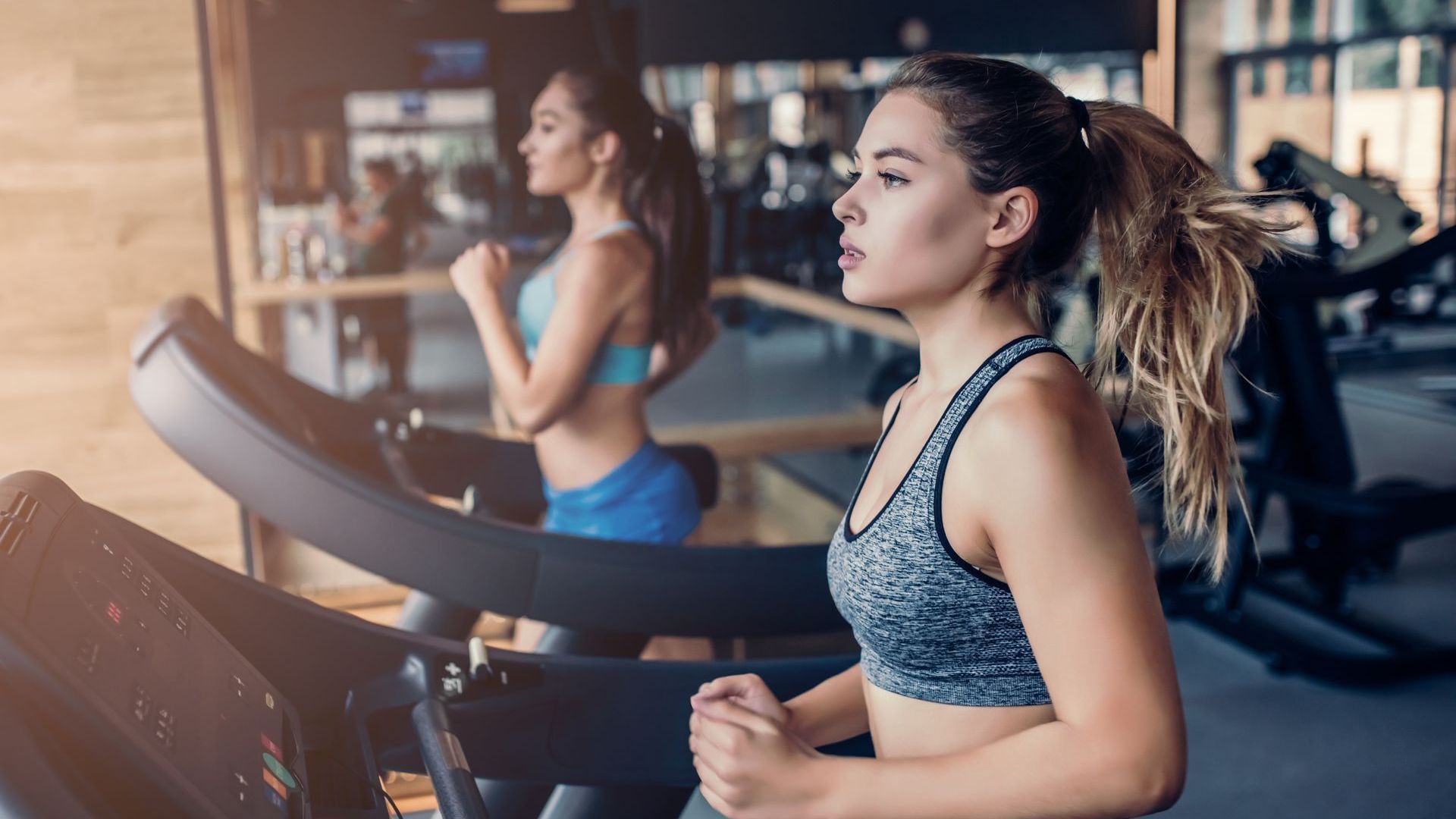 Two women are running on treadmills in a gym.