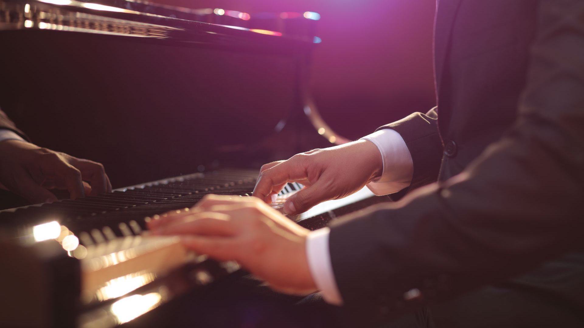 A man in a suit is playing a piano in a dark room.