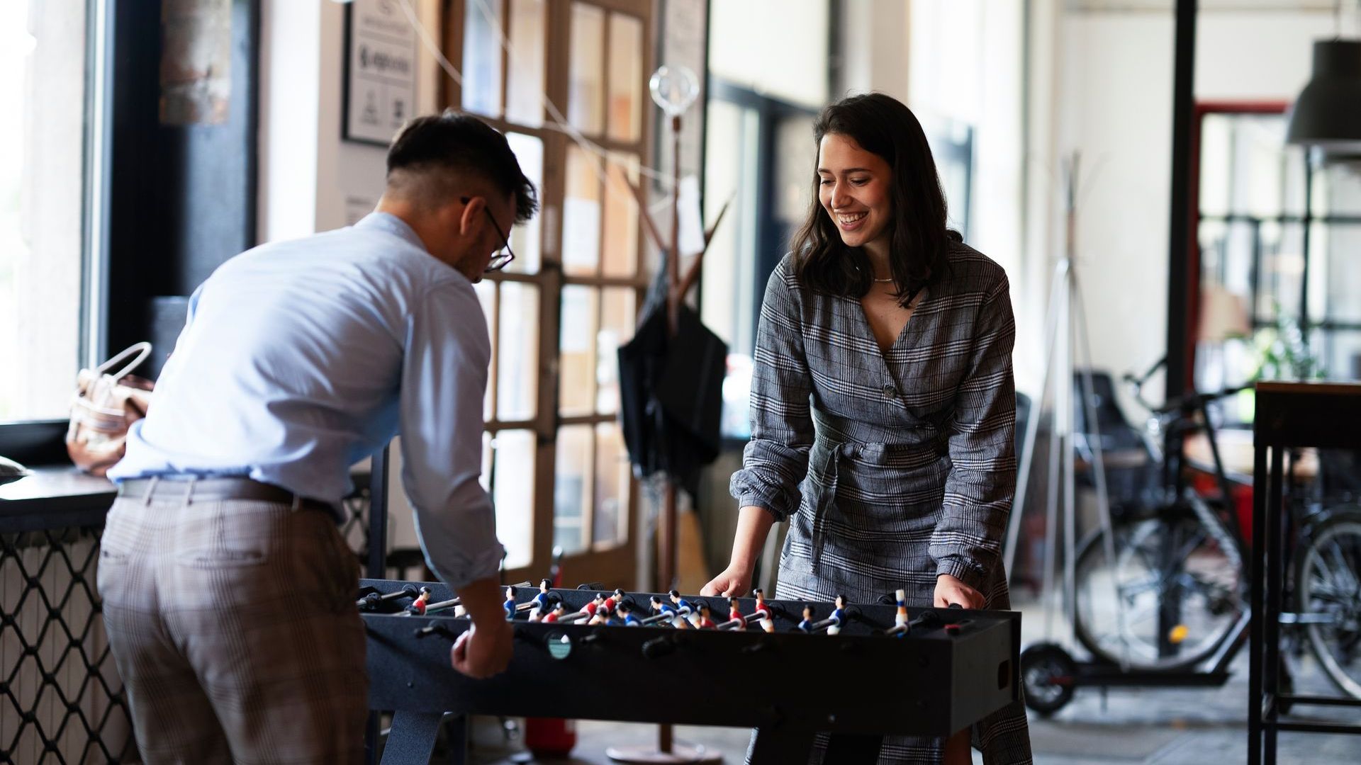 A man and a woman are playing foosball in an office.