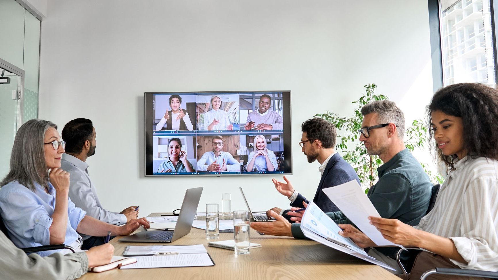A group of people are sitting around a table having a video conference.