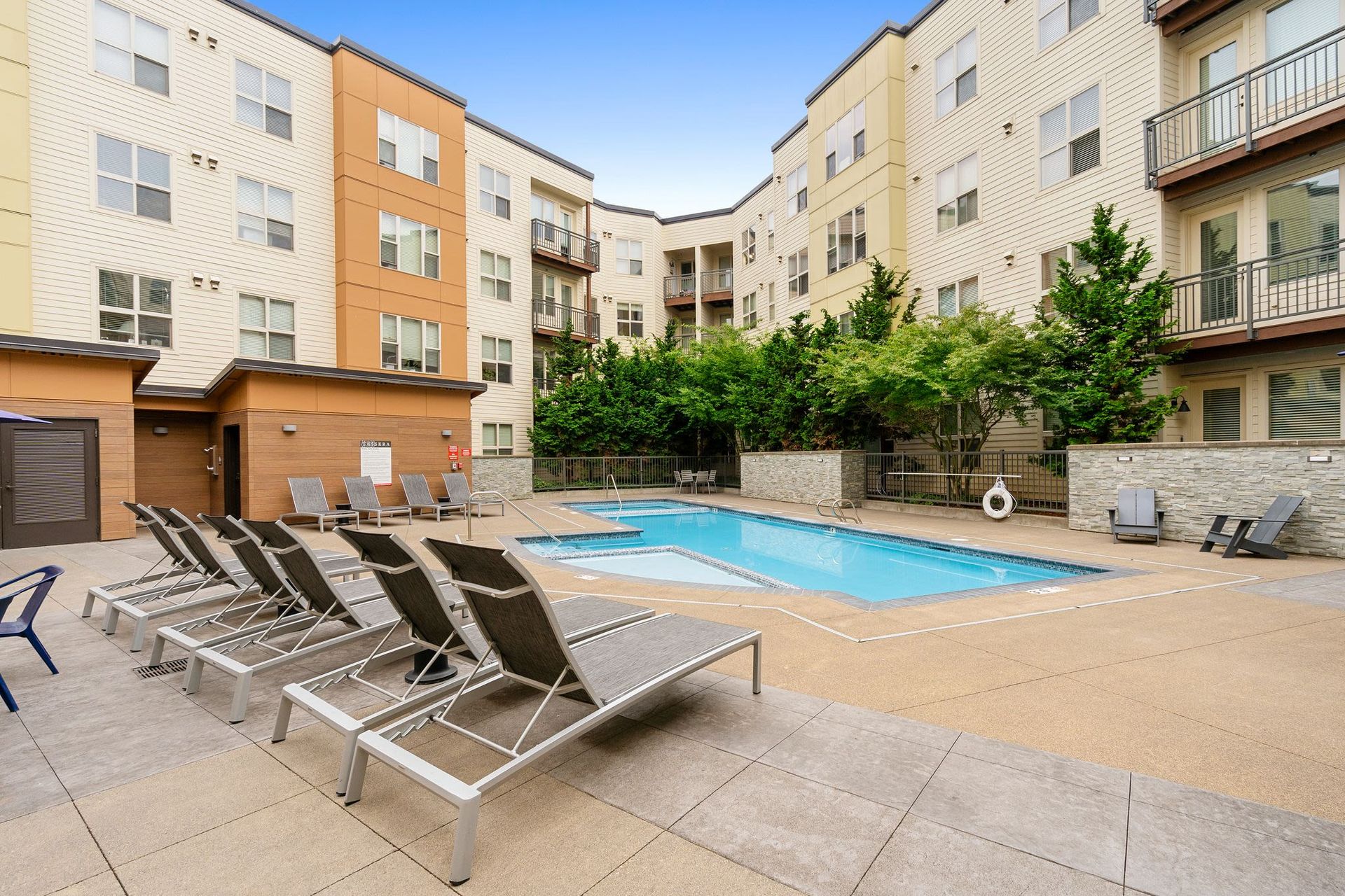 Outdoor pool area at an apartment community with lounge chairs and surrounding buildings at Tessera at Orenco Station.