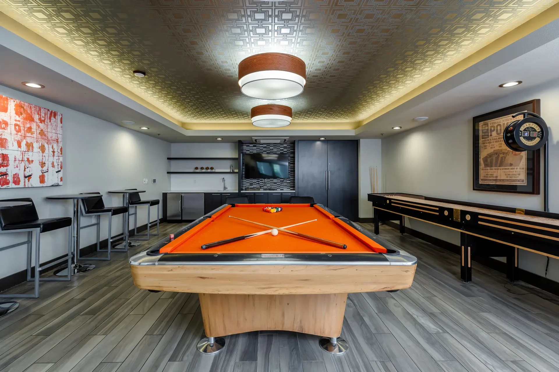 Indoor recreation room with an orange pool table, foosball table, and bar-height seating at Tessera at Orenco Station.