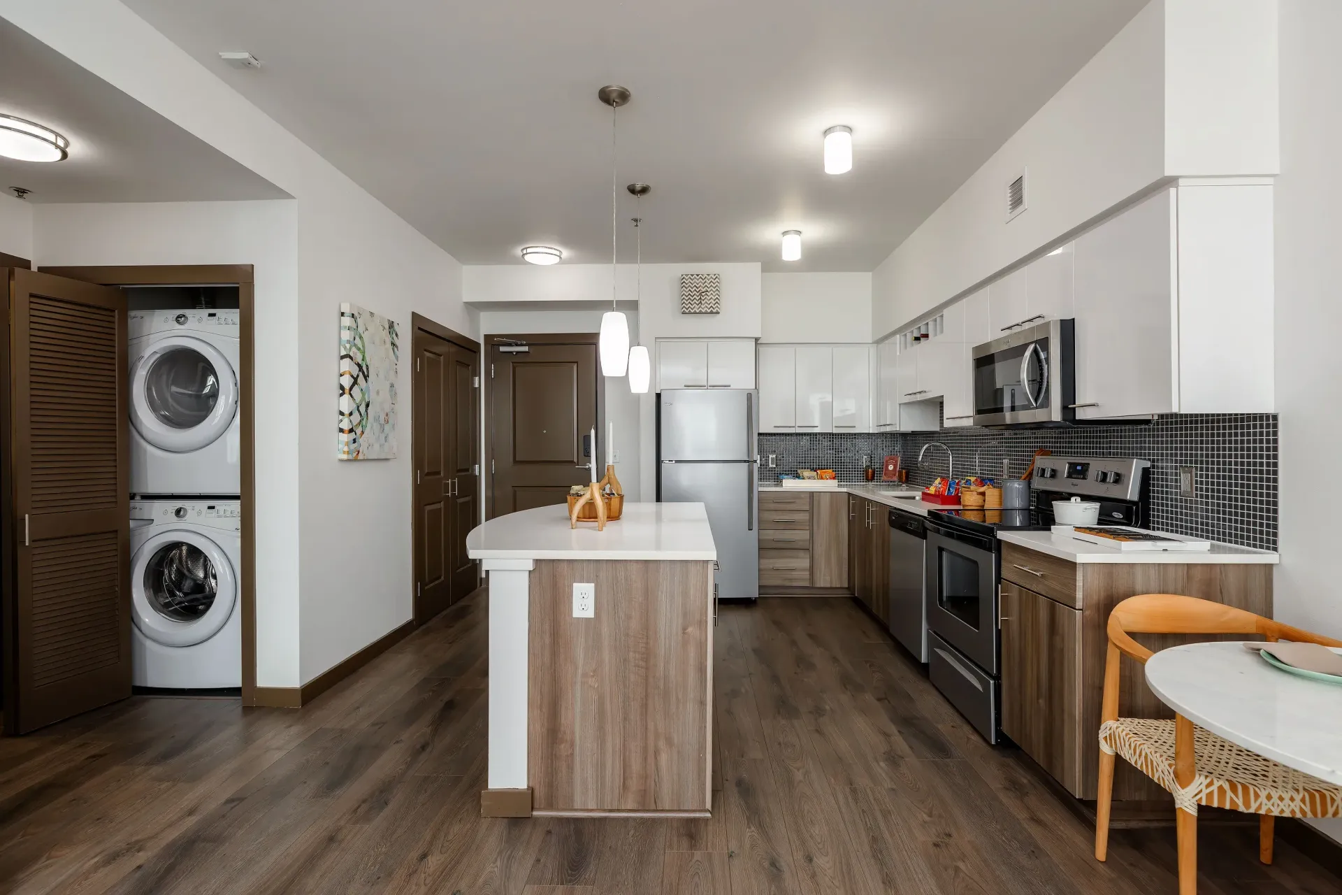 Open-concept kitchen with an island, stainless steel appliances, and a stacked washer/dryer in a closet at Tessera at Orenco Station.