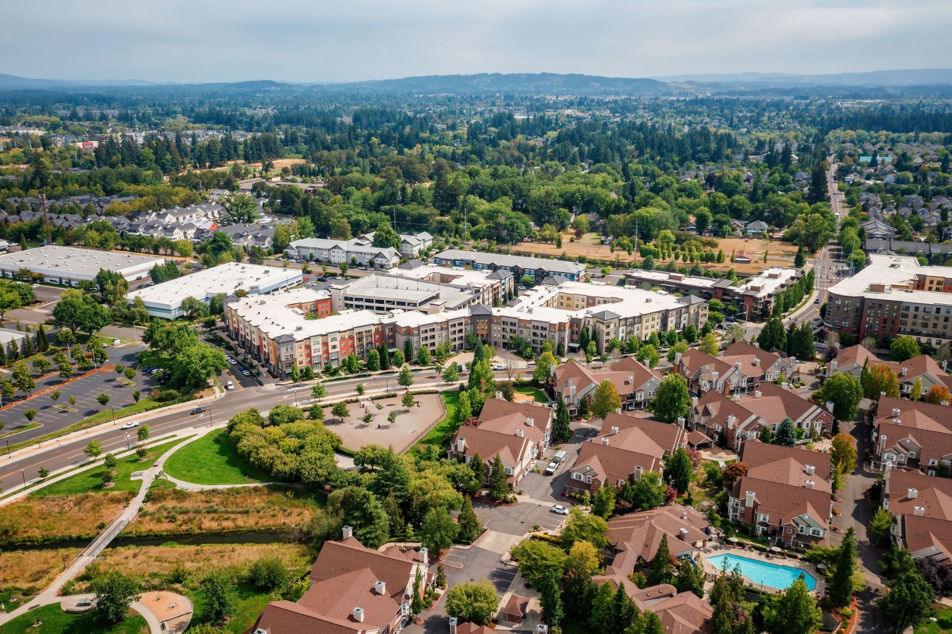 Aerial view of a suburban multifamily community with interconnected mid-rise buildings and a visible pool at Tessera at Orenco Station.