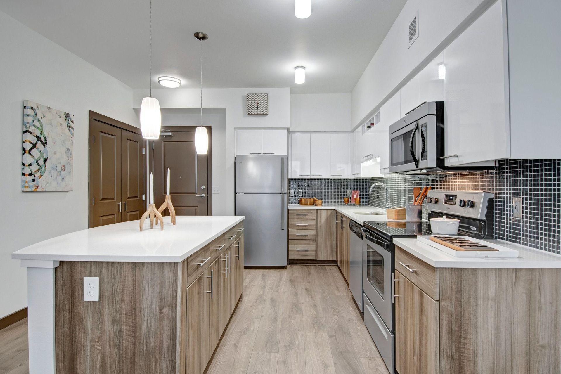 Modern kitchen in apartment with island, white cabinetry, and stainless steel appliances at Tessera at Orenco Station.