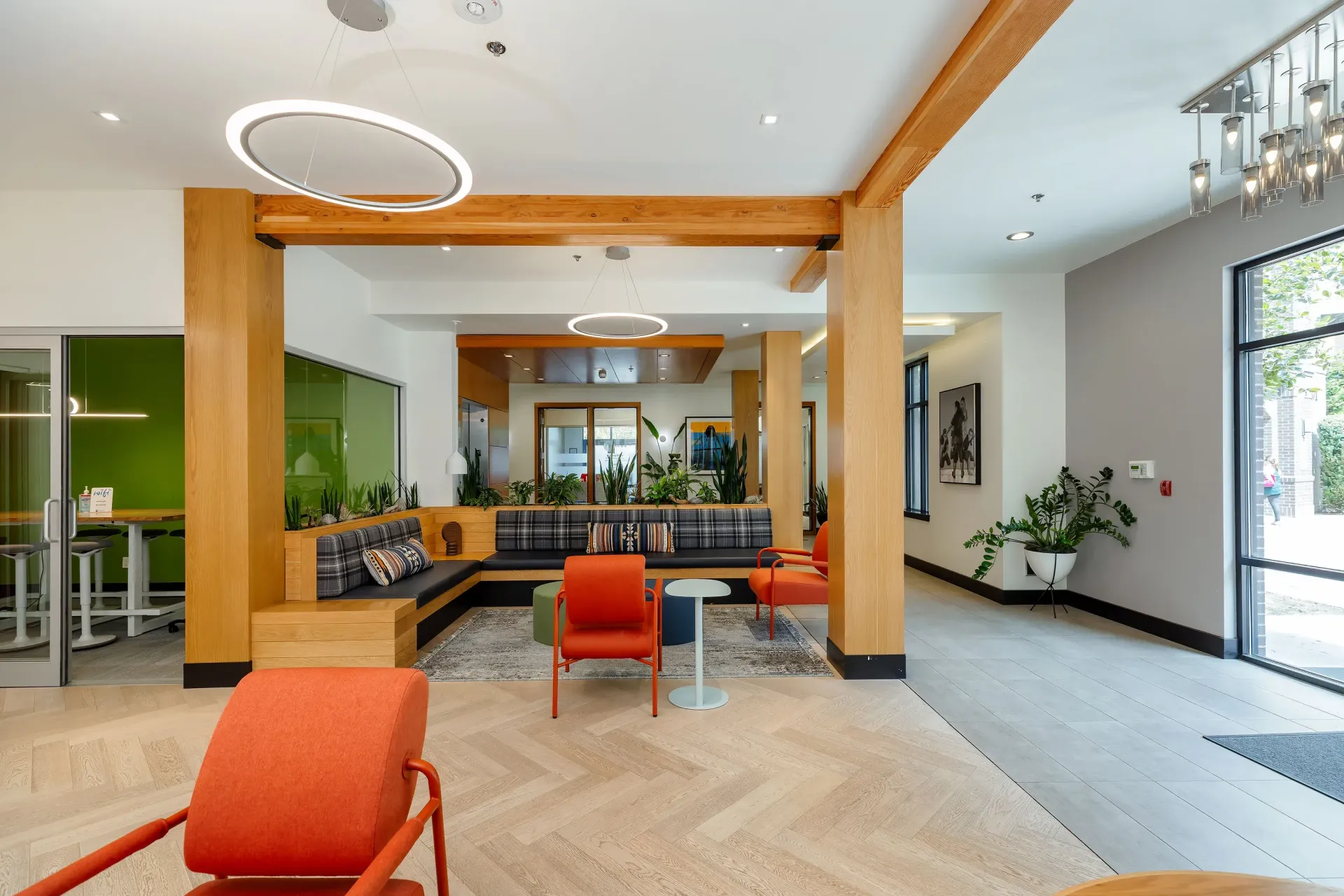 Bright apartment lobby with wood beams, orange seating, and green plants.